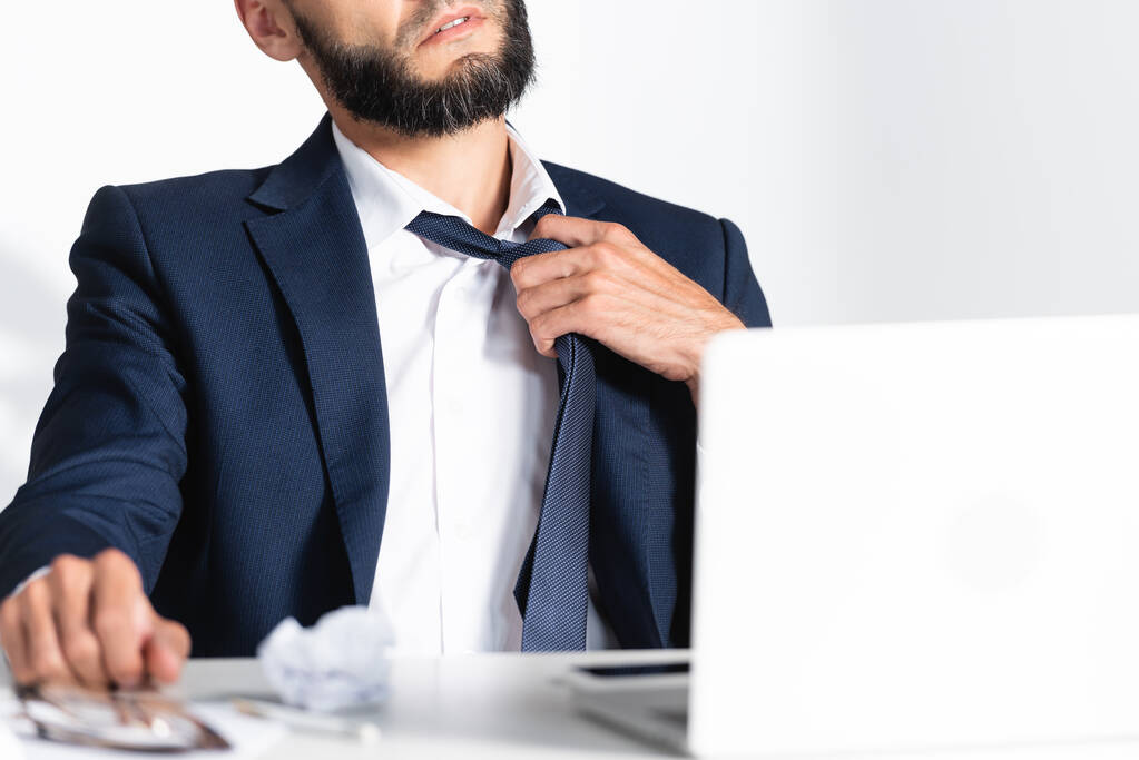 Cropped view of businessman touching tie while feeling hot near laptop on blurred foreground  - Photo, Image