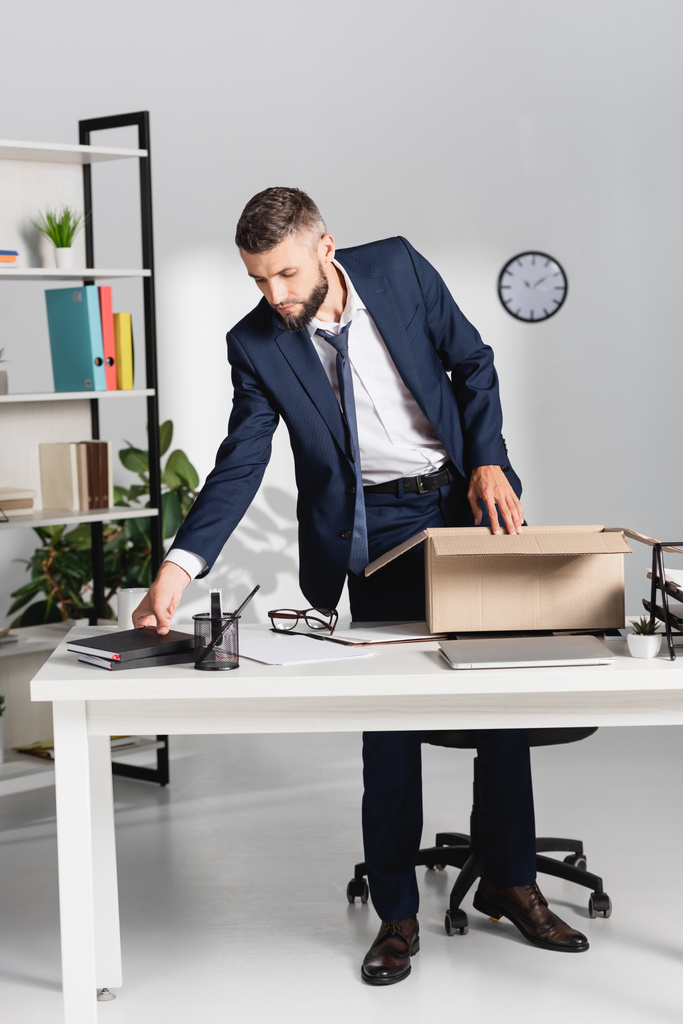 Dismissed businessman taking notebook near laptop and cardboard box in office  - Photo, Image