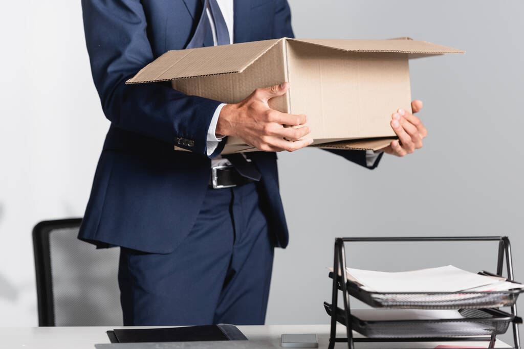 Vista ritagliata dell'uomo d'affari licenziato che tiene la scatola di cartone vicino ai documenti in primo piano sfocata  - Foto, immagini