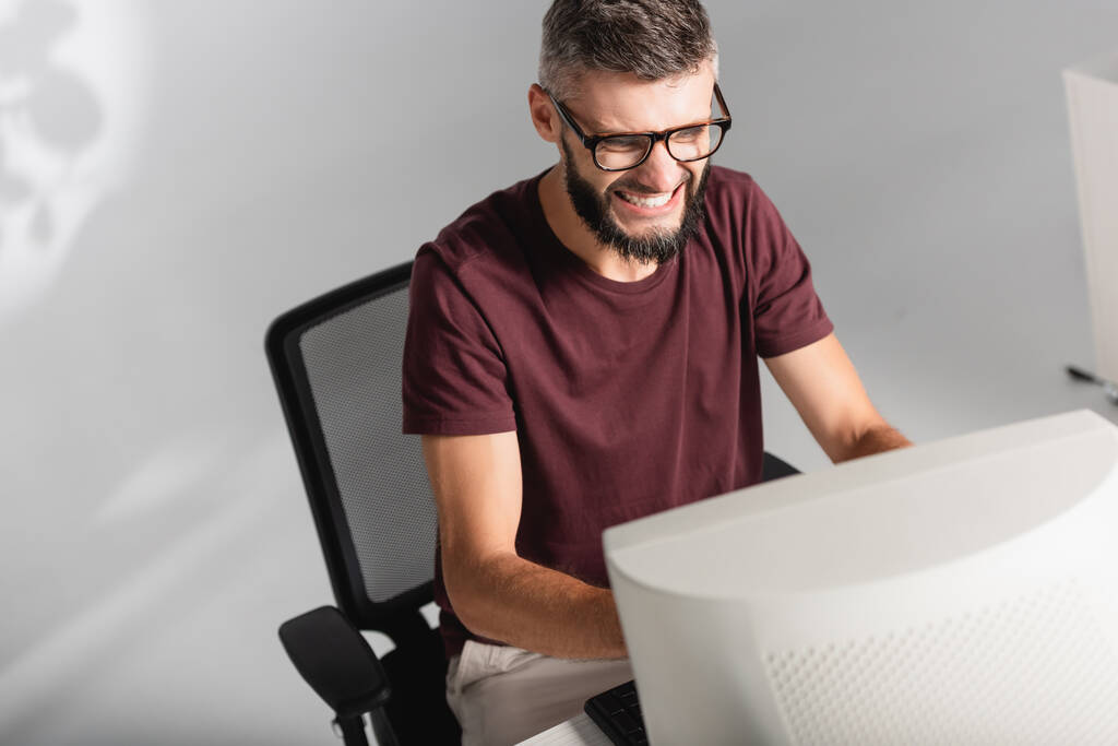 Aggressiver Geschäftsmann sitzt im Büro neben Computer im verschwommenen Vordergrund  - Foto, Bild