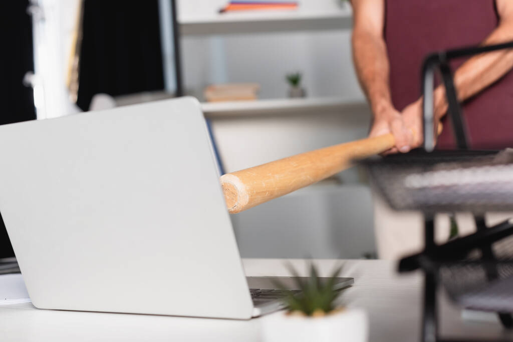 Vágott kilátás üzletember kezében baseball ütő közelében laptop elmosódott előtér irodai asztal  - Fotó, kép