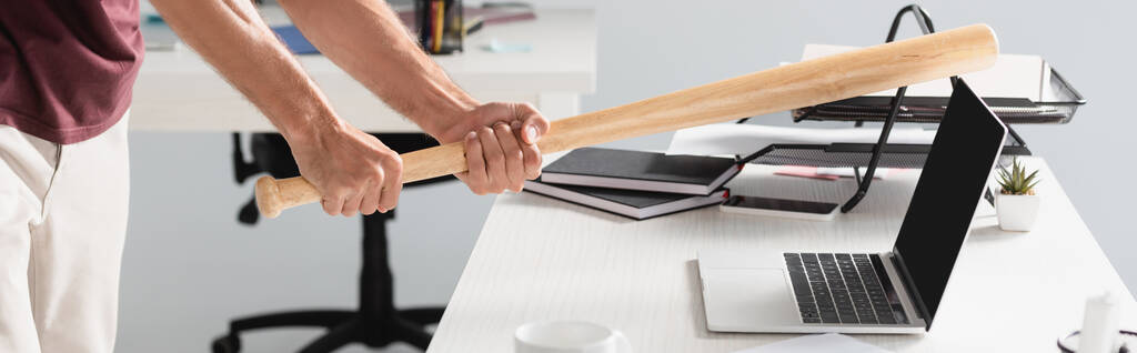Vista cortada de empresário batendo laptop com bastão de beisebol com fundo embaçado no escritório, banner  - Foto, Imagem