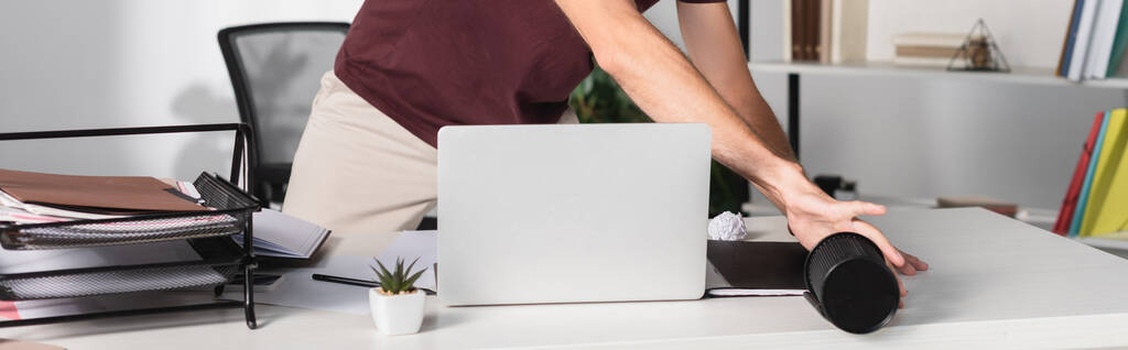Ausgeschnittene Ansicht eines Geschäftsmannes, der Laptop und Schreibwaren vom Tisch im Büro wirft, Banner  - Foto, Bild