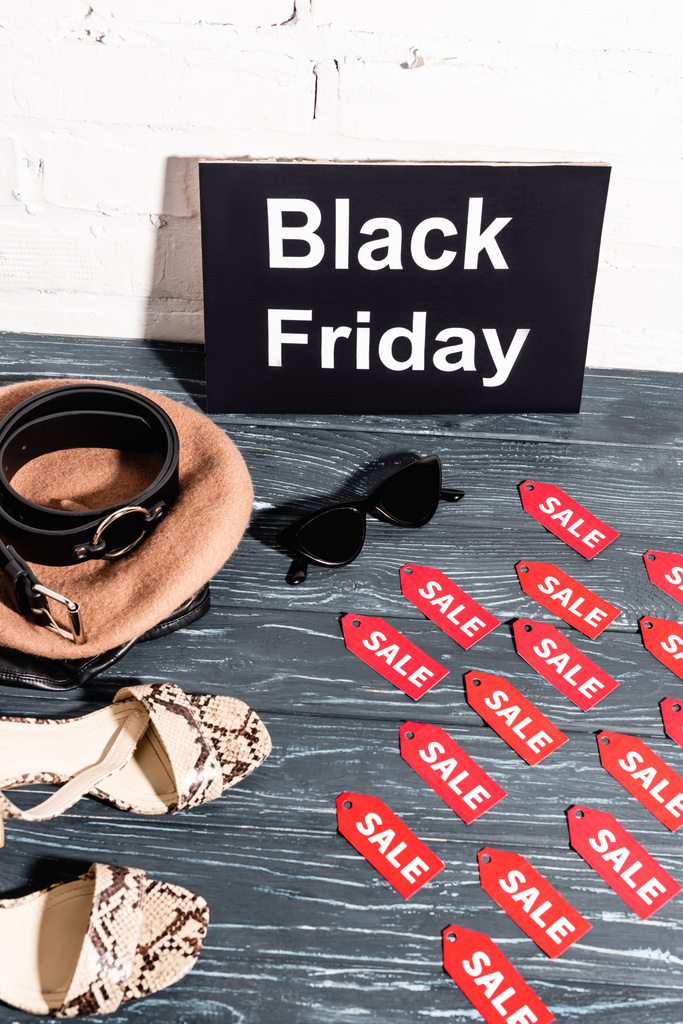 Schuhe, Sonnenbrille, Baskenmütze und Gürtel in der Nähe Bord mit schwarzem Freitag und Tags mit Verkauf Schriftzug auf der Oberfläche - Foto, Bild