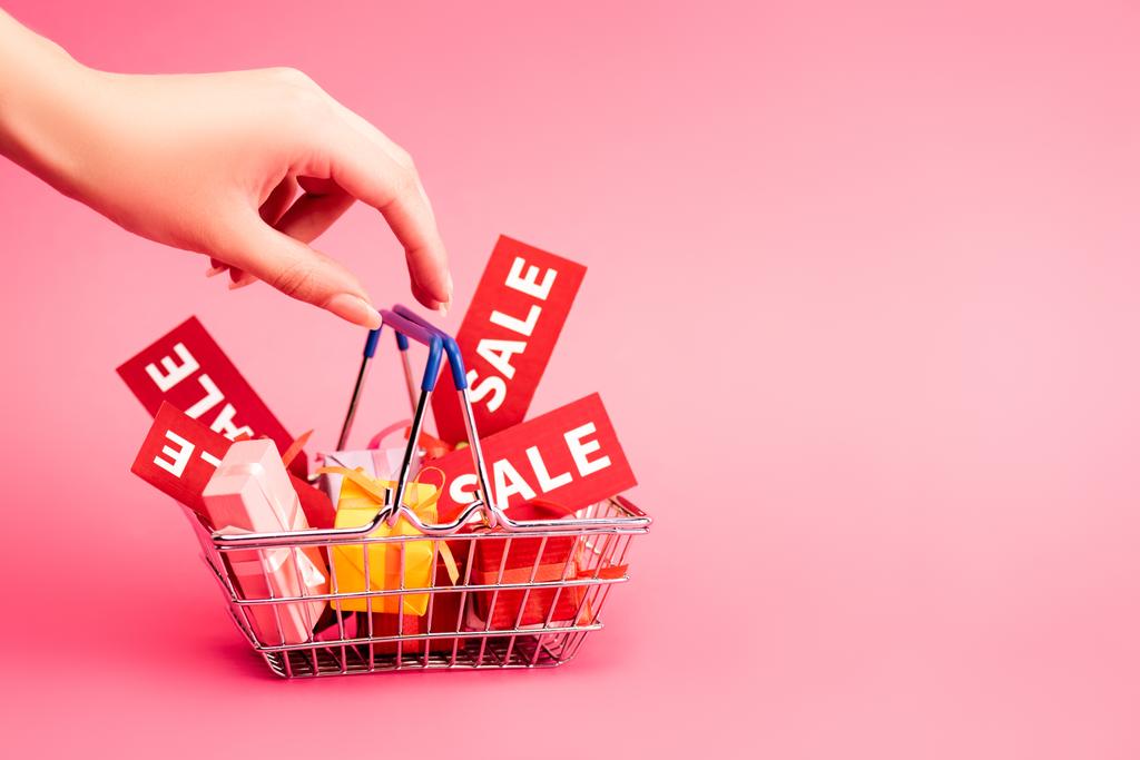 cropped view of female hand near shopping basket with gifts and red tag with lettering on pink, black friday concept - Photo, Image