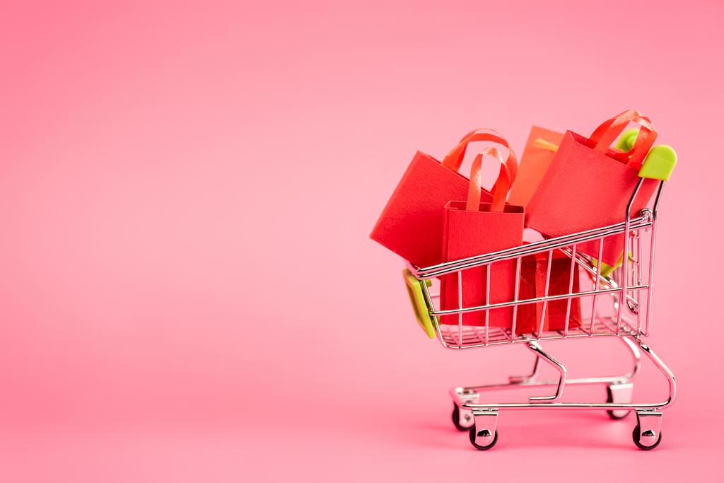 Einkaufstaschen im kleinen Einkaufswagen auf rosa, schwarzem Freitag-Konzept  - Foto, Bild