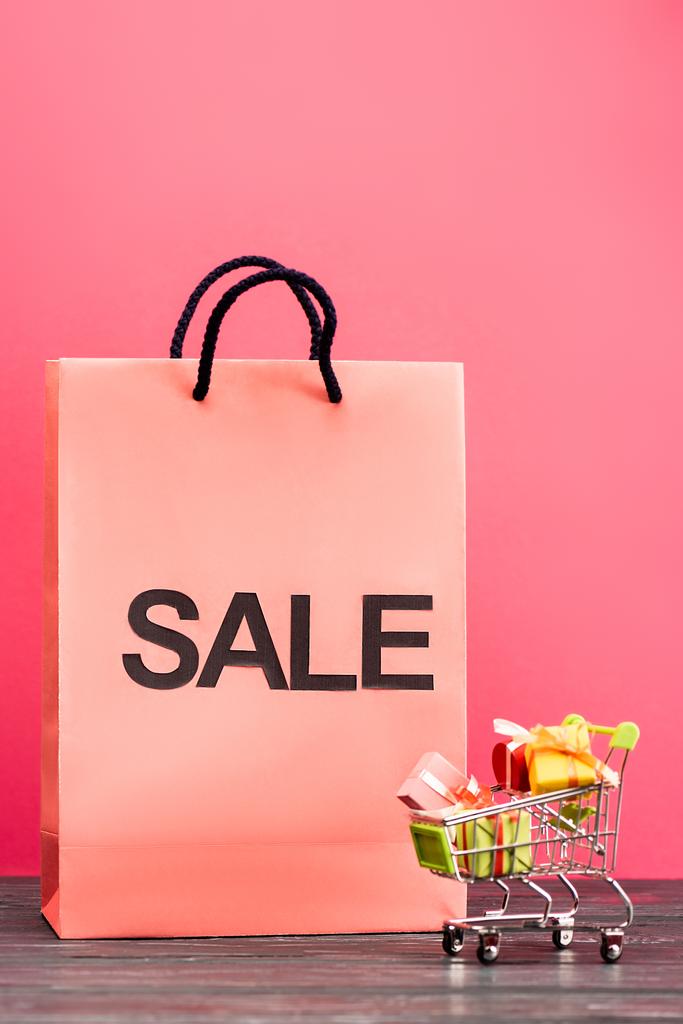 сумка с надписью продажи рядом с небольшой тележки с подарками на розовый, черный пятница концепции  - Фото, изображение