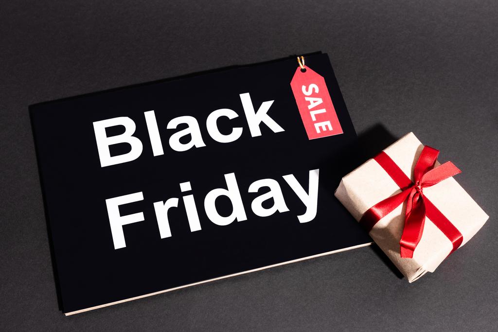 bovenaanzicht van geschenkdoos met lint en sale tag bij zwart vrijdagbordje op donkere achtergrond - Foto, afbeelding