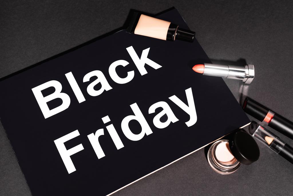 high angle view of placard with black friday lettering near decorative cosmetics on dark background - Photo, Image