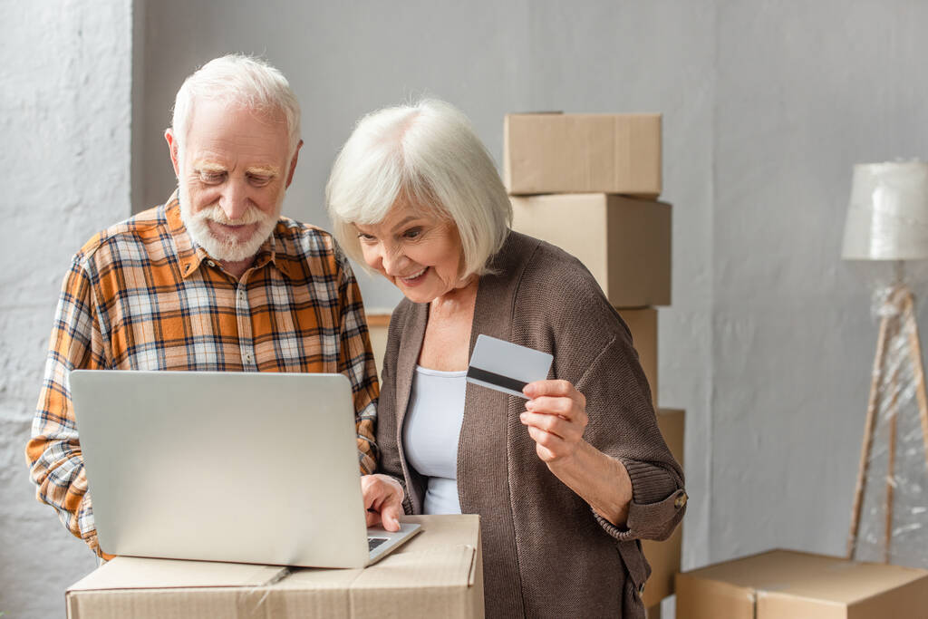 Lächelndes Senioren-Paar kauft online mit Laptop und Kreditkarte ein - Foto, Bild