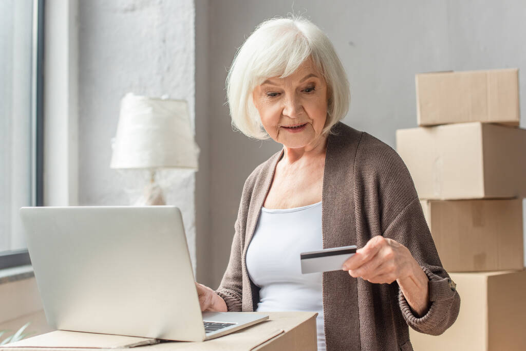 vanhempi nainen tekee verkko-ostoksia luottokortilla ja kannettavalla tietokoneella - Valokuva, kuva