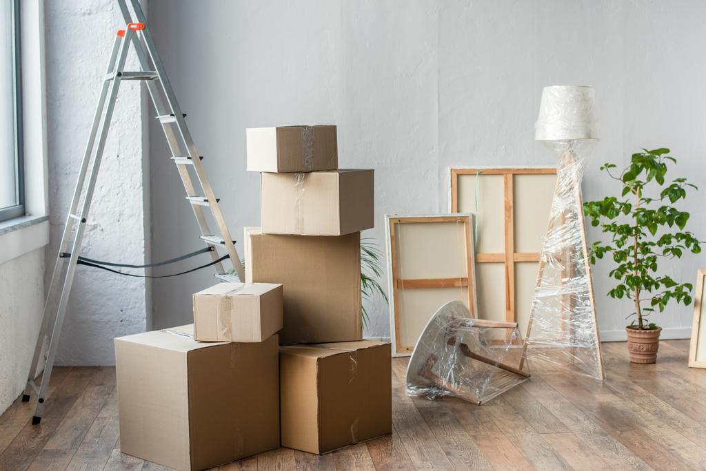 kartonnen dozen, lijsten, ladder, lamp en installatie in lege ruimte, bewegend concept - Foto, afbeelding
