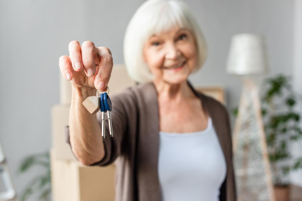 θολή άποψη του χαμογελαστού ηλικιωμένη γυναίκα κρατώντας κλειδιά, κινούμενη έννοια - Φωτογραφία, εικόνα