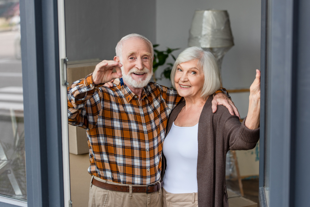 laughing senior man holding keys and embracing wife in new house - Photo, Image