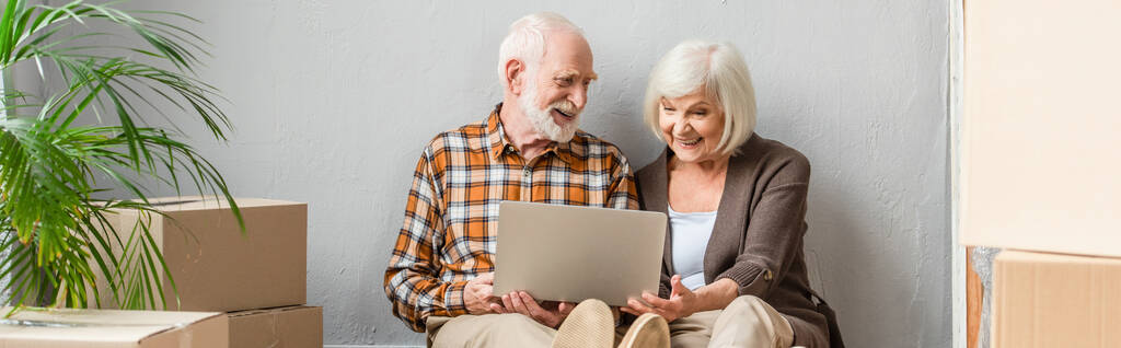 colpo panoramico di coppia anziana utilizzando computer portatile seduto al piano - Foto, immagini