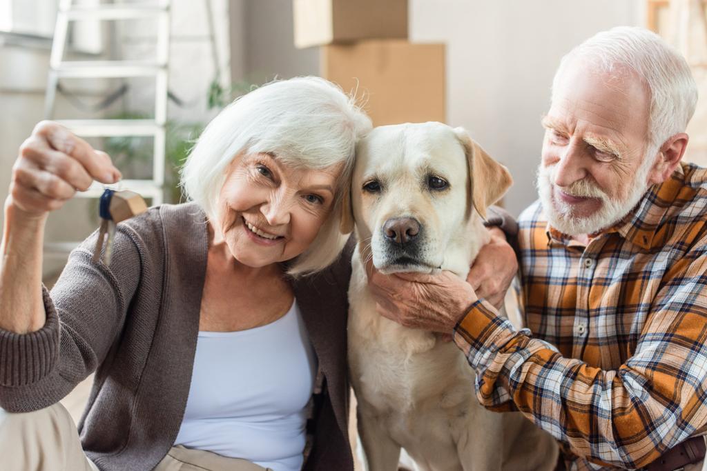 idős férfi simogatás kutya míg feleség gazdaság kulcsok, mozgó koncepció - Fotó, kép