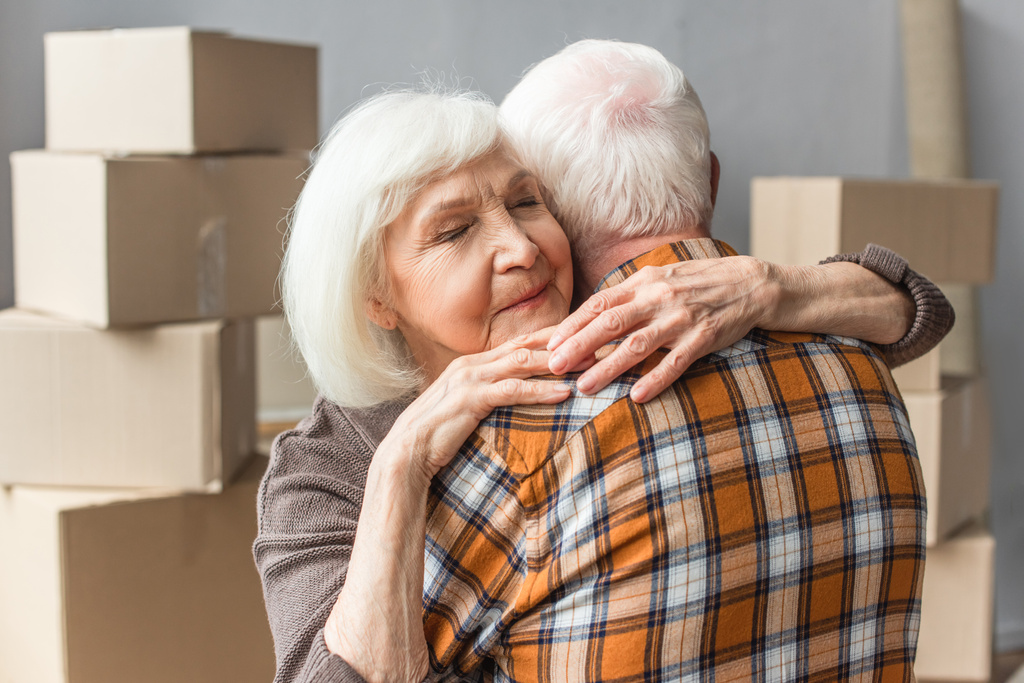 mulher idosa com olhos fechados abraçando o marido na nova casa, conceito em movimento - Foto, Imagem