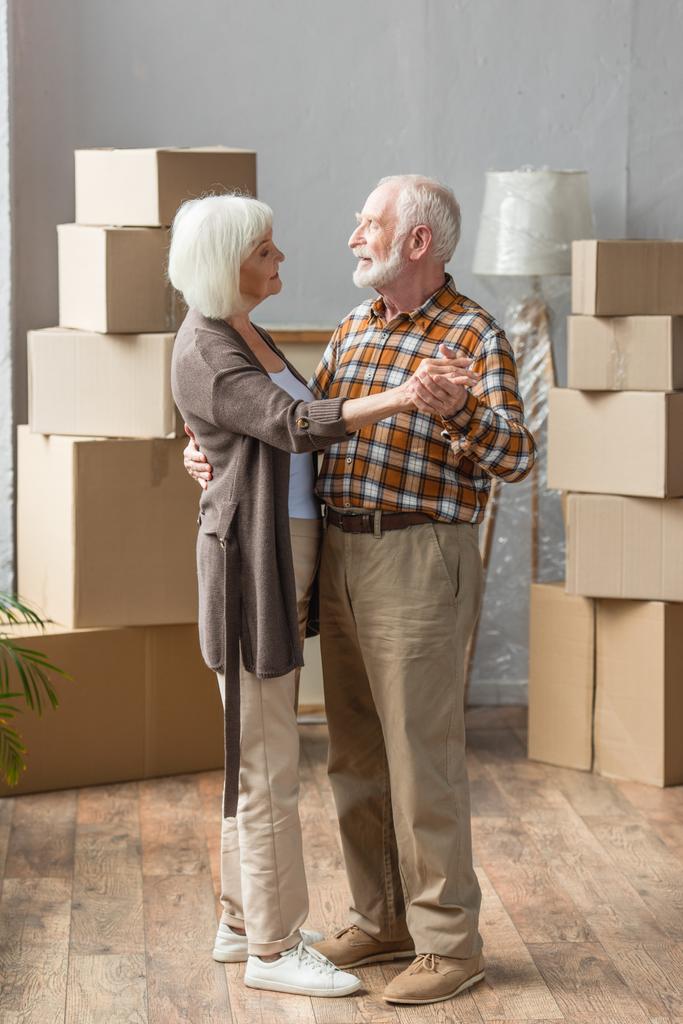plná délka pohled na veselý starší pár tanec v novém domě s lepenkovými krabicemi na pozadí - Fotografie, Obrázek