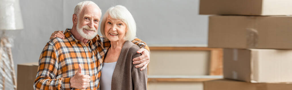 Panoramaaufnahme von Senioren-Paar umarmt und Mann zeigt Schlägerei in neuem Haus, bewegendes Konzept - Foto, Bild