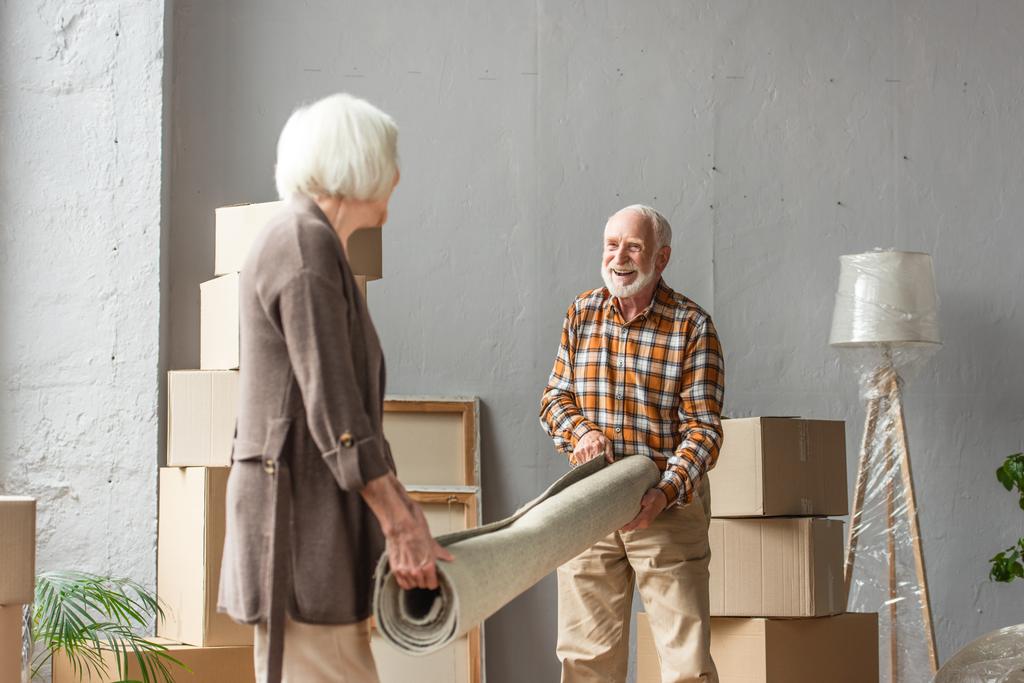 Lächelndes Seniorenpaar rollt Teppich in neuem Haus, bewegendes Konzept - Foto, Bild