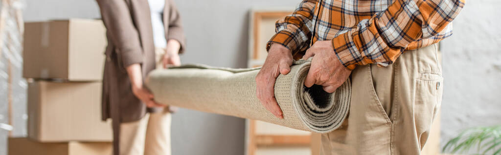 Panoramaaufnahme eines Senioren-Ehepaares, das Teppich in neuem Haus rollt, bewegendes Konzept - Foto, Bild