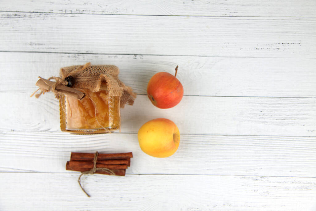 glazen pot jam, appels en kaneel op witte houten ondergrond plat gelegd. Afbeelding bevat kopieerruimte - Foto, afbeelding