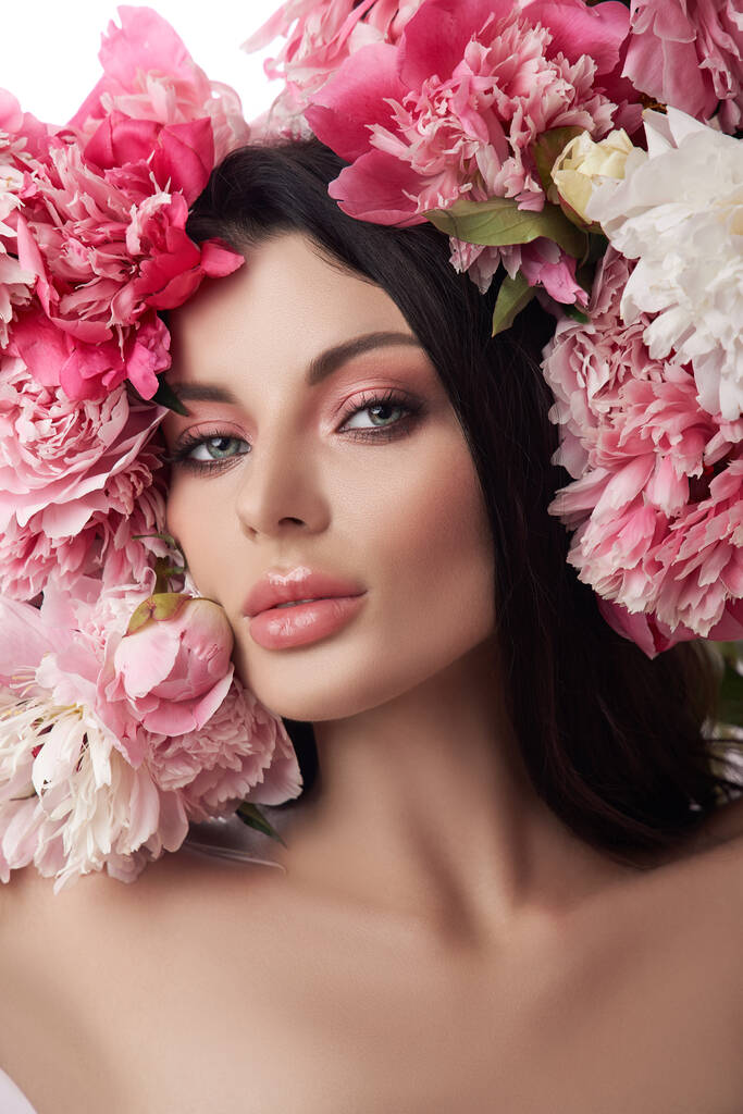 Bella donna bruna con fiori di peonia. Cosmetici naturali e trucco, pelle perfetta - Foto, immagini