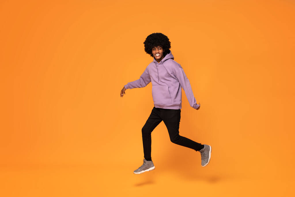 Homme heureux avec des cheveux afro sautant sur fond orange. - Photo, image