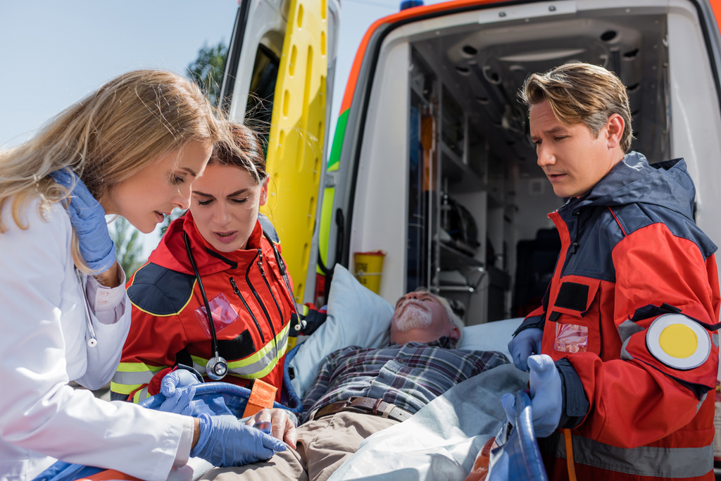 Выборочный фокус врача и парамедика, смотрящего на пациента на носилках возле машины скорой помощи на открытом воздухе  - Фото, изображение