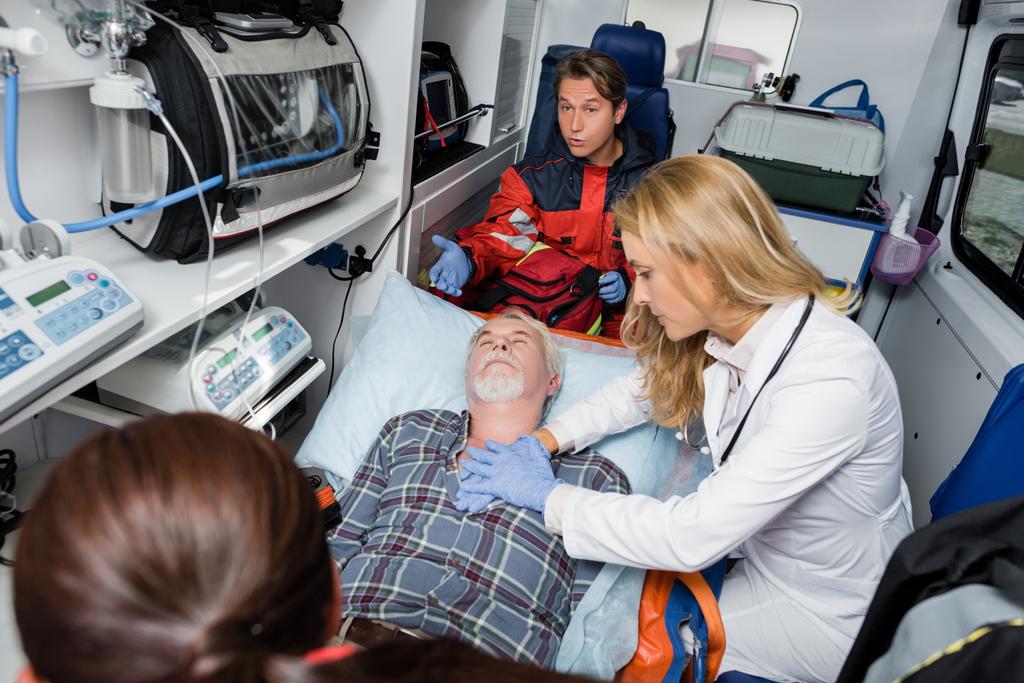 Selektywne skupienie się lekarza w rękawiczkach lateksowych wykonującego resuscytację sercowo-płucną u pacjenta w pobliżu sanitariuszy w wagonie karetki  - Zdjęcie, obraz