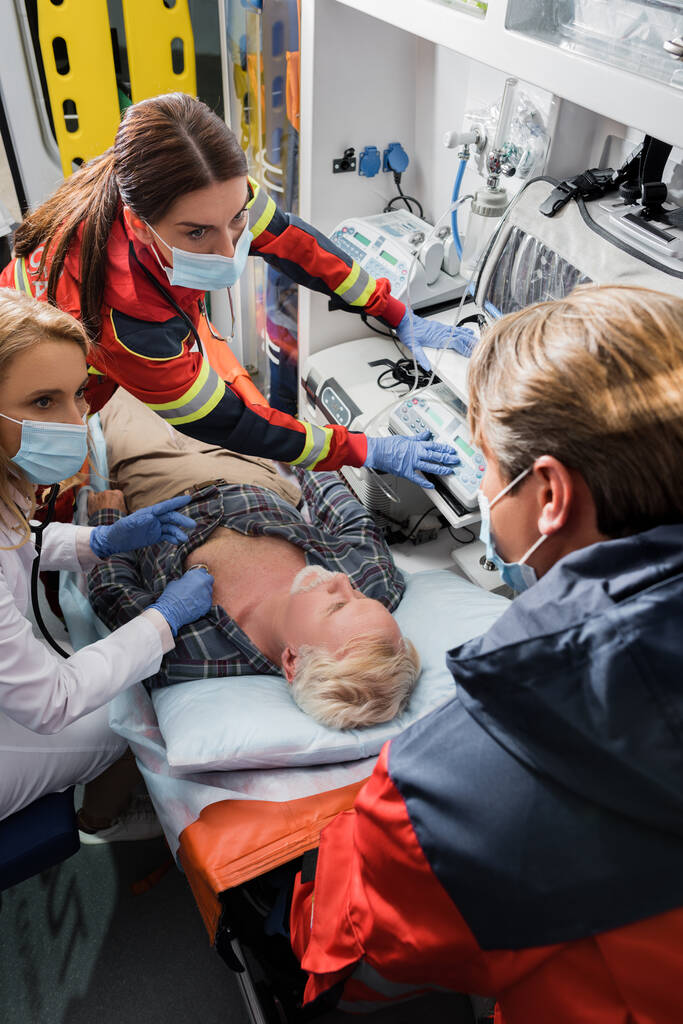 Focus selettivo di paramedici e medici in maschere mediche che fanno pronto soccorso a pazienti malati in ambulanza  - Foto, immagini