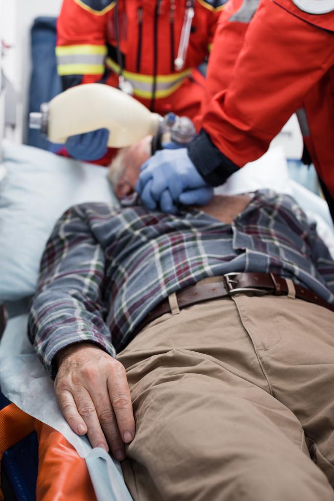 Επιλεκτική εστίαση του ηλικιωμένου που βρίσκεται σε ασθενοφόρο κοντά σε παραϊατρικό προσωπικό που κάνει καρδιοπνευμονική ανάνηψη - Φωτογραφία, εικόνα