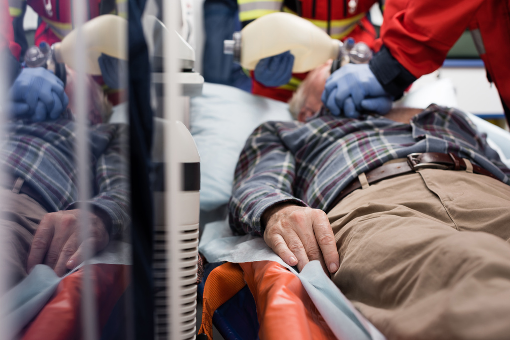 Sağlık görevlileri kardiyopulmoner resüsitasyon yaparken yaşlı bir hastanın ambulans arabasında yatmasının seçici odak noktası - Fotoğraf, Görsel