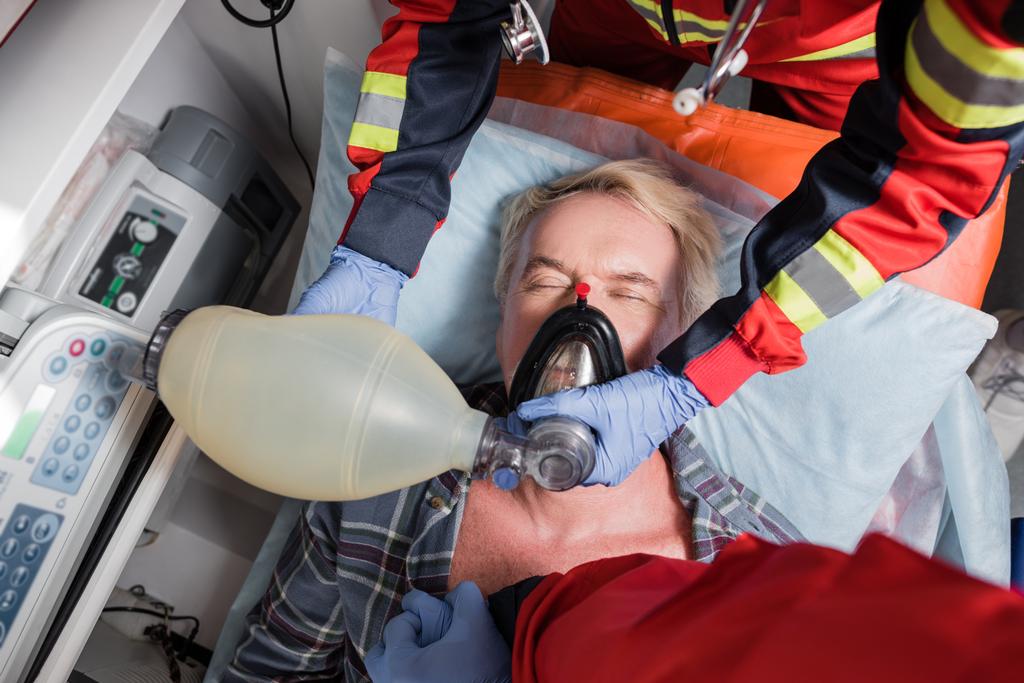 Visão superior de paramédicos em luvas de látex fazendo ressuscitação cardiopulmonar para homem idoso  - Foto, Imagem