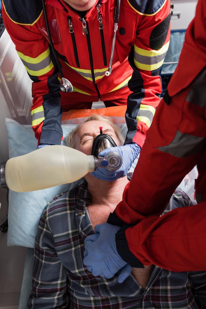 Vista dall'alto dei paramedici in guanti di lattice che fanno rianimazione cardiopolmonare all'uomo anziano in auto ambulanza  - Foto, immagini