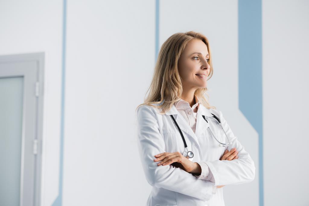 Blonde médecin avec les bras croisés regardant loin dans la clinique  - Photo, image