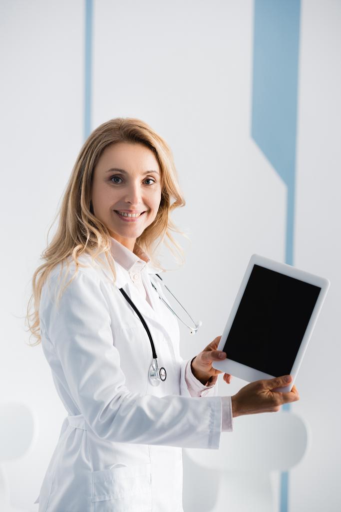 Ξανθός γιατρός δείχνει ψηφιακό δισκίο με λευκή οθόνη στην κλινική - Φωτογραφία, εικόνα