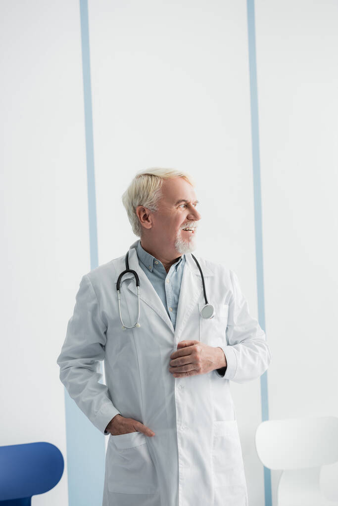 Medico dai capelli grigi che distoglie lo sguardo mentre lavora in ospedale  - Foto, immagini