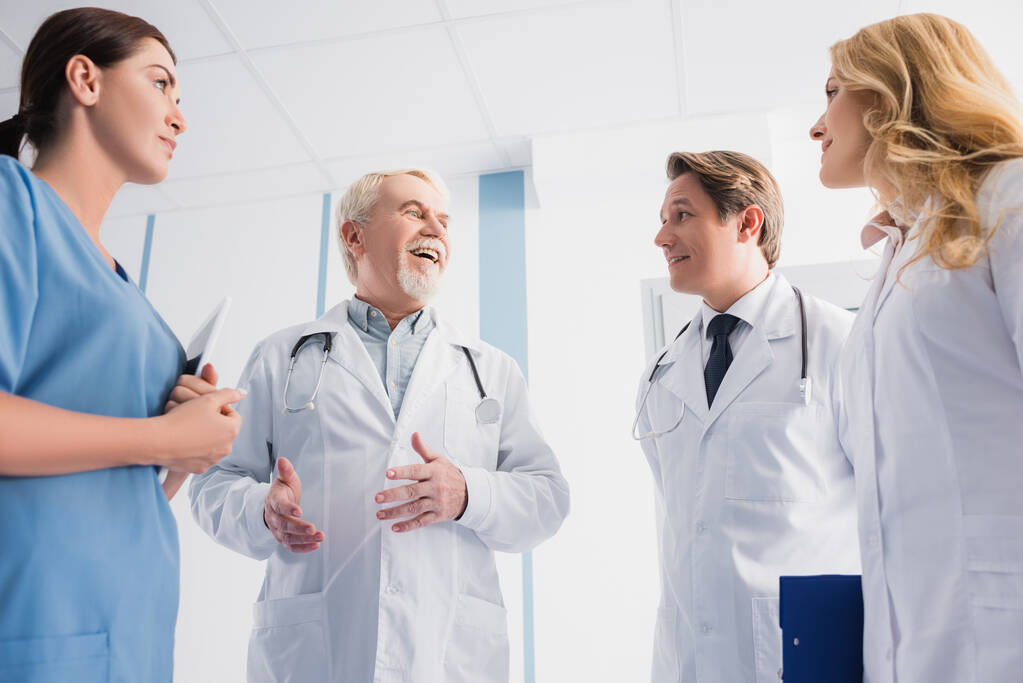 Doktorların ve dijital tabletli hemşirelerin seçici odağı hastanede konuşurken meslektaşlarına bakıyorlar.  - Fotoğraf, Görsel