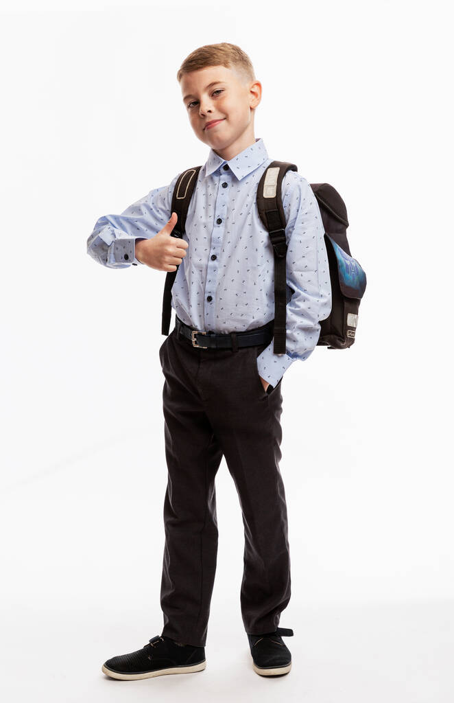 Iskolásfiú egyenruhában, hátizsákos mosollyal és feltartott hüvelykujjal. Vissza a suliba. Teljes magasság. Fehér háttér. Függőleges. - Fotó, kép