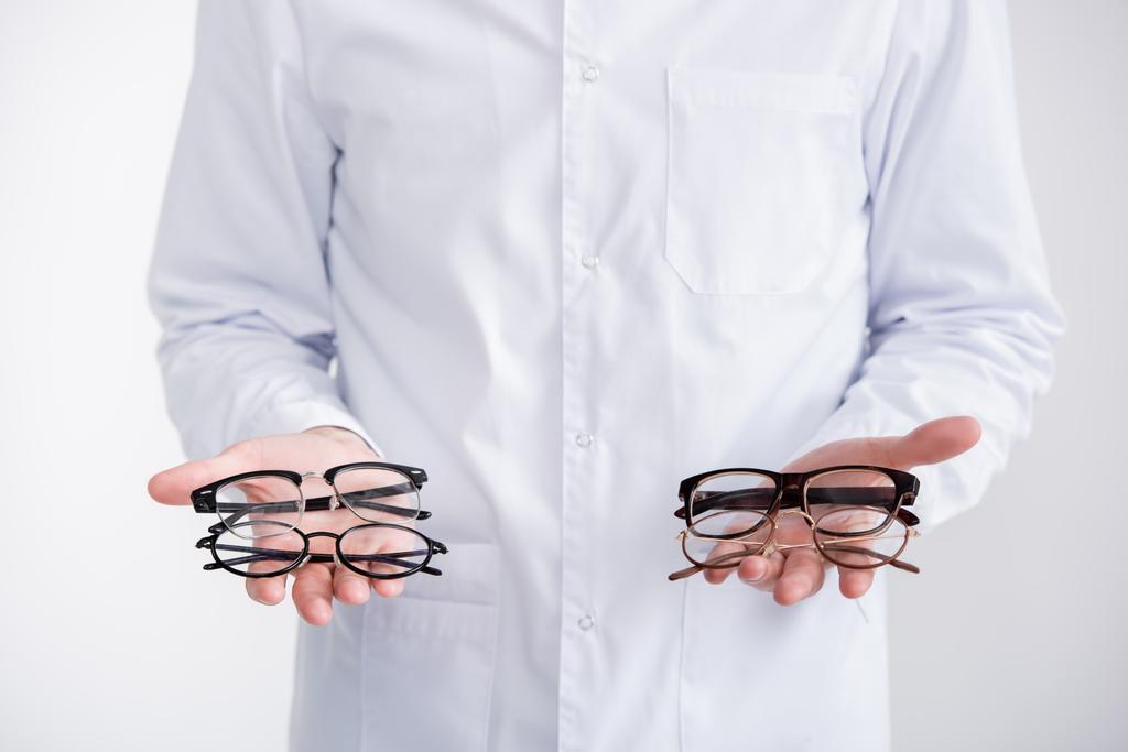 Обрезанный вид врача, показывающий пары очков на ладонях, изолированных на белом - Фото, изображение