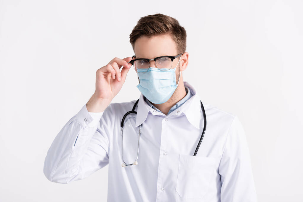 Widok z przodu lekarza w masce medycznej, trzymając ramę okularów na parze izolowane na białym - Zdjęcie, obraz