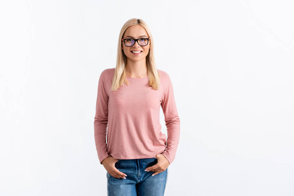 Front view of happy blonde woman with hands in pockets, wearing eyeglasses and looking at camera isolated on white - Photo, Image