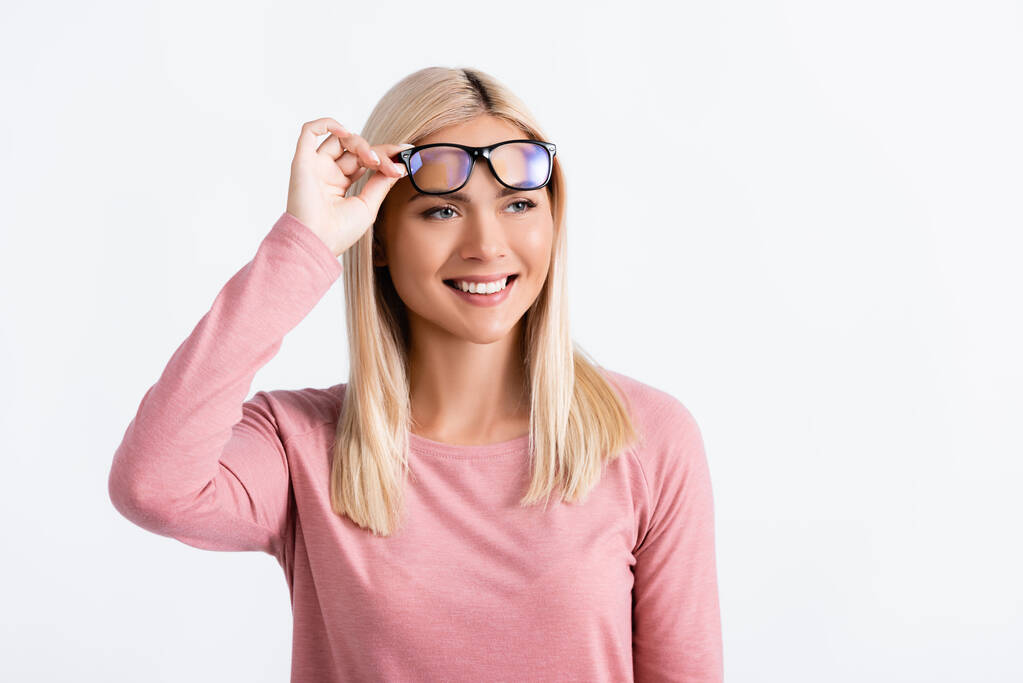 Blondýny žena se usmívá, zatímco drží brýle izolované na šedé - Fotografie, Obrázek