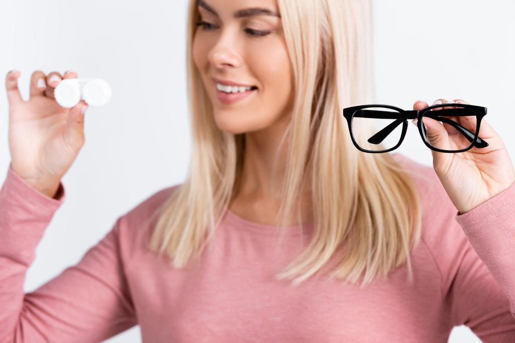 Eyeglasses in hand of smiling woman holding container with contact lenses on blurred background isolated on grey - Photo, Image