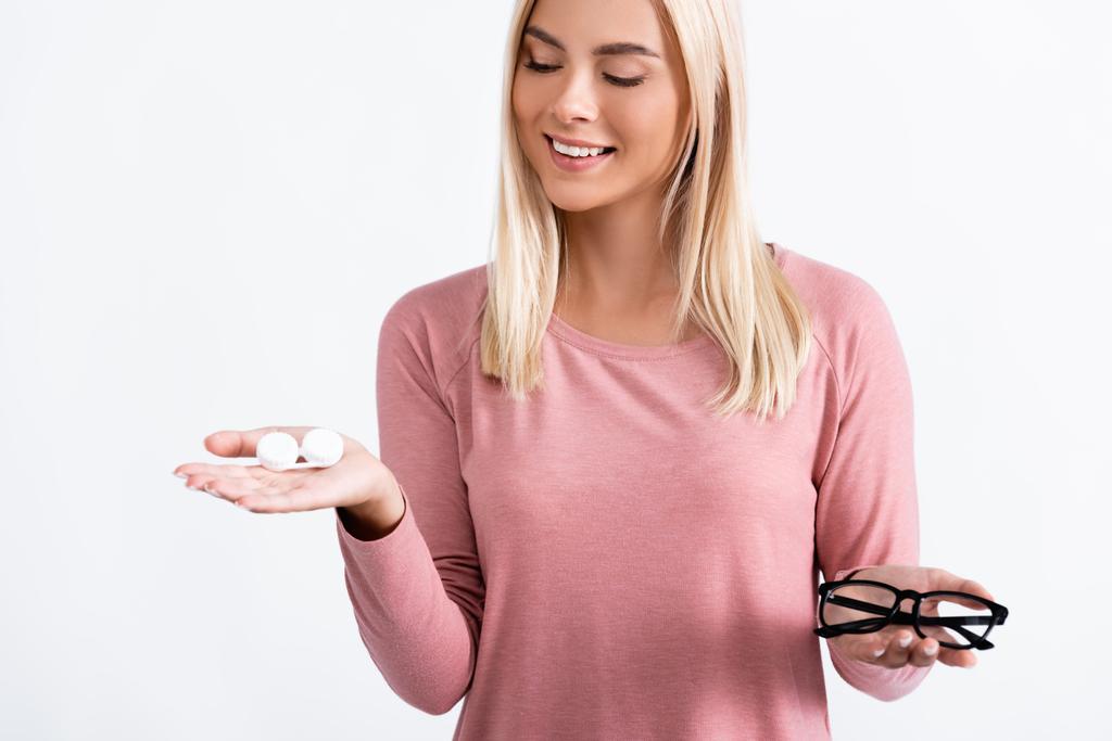 Jonge vrouw kijkt naar doos met contactlenzen terwijl ze een bril op wit houdt - Foto, afbeelding