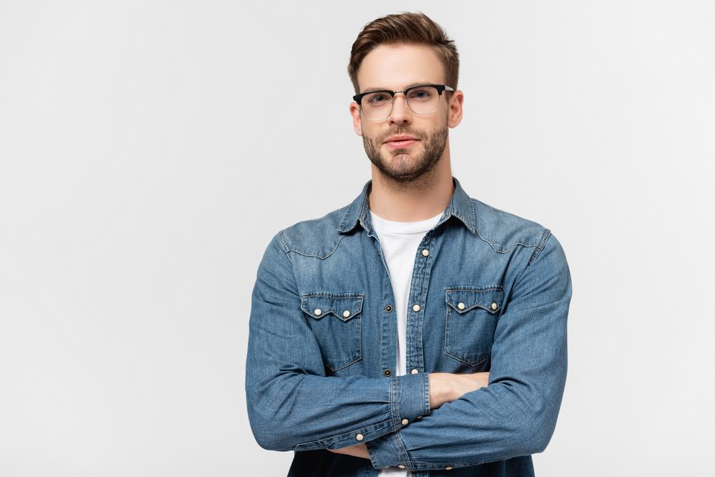Young man in eyeglasses looking at camera while standing with crossed arms isolated on grey - Photo, Image