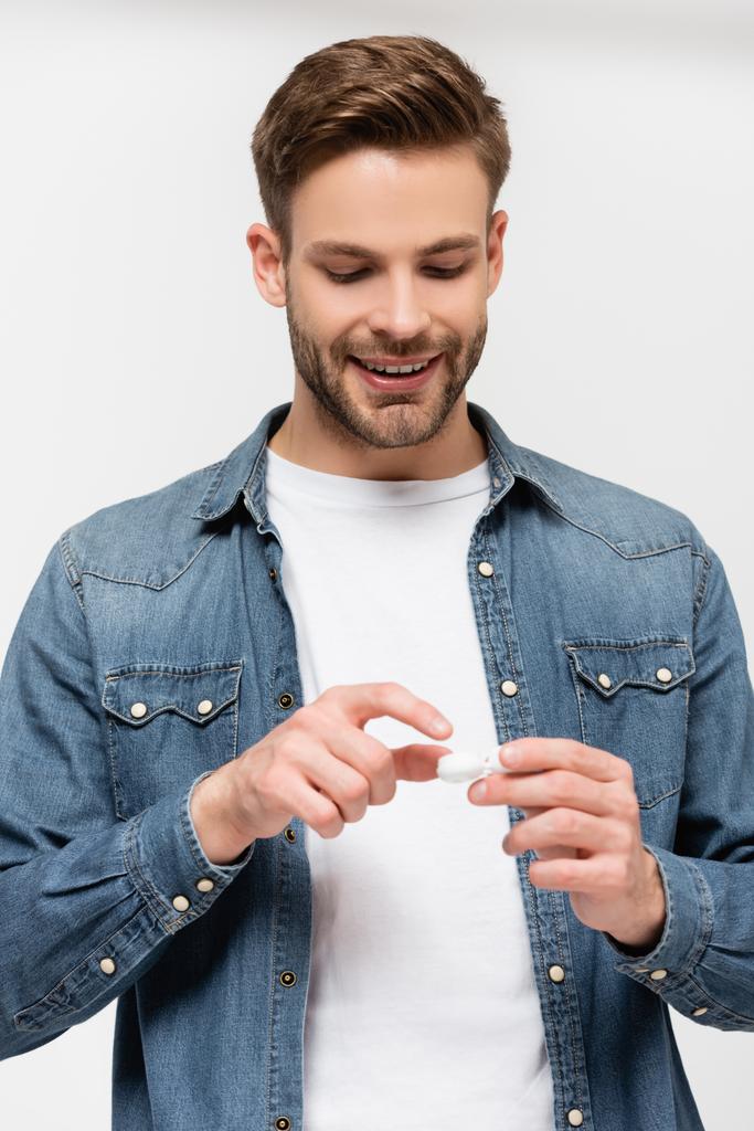 Молодой улыбающийся мужчина держит контейнер с контактными линзами, изолированными на сером - Фото, изображение