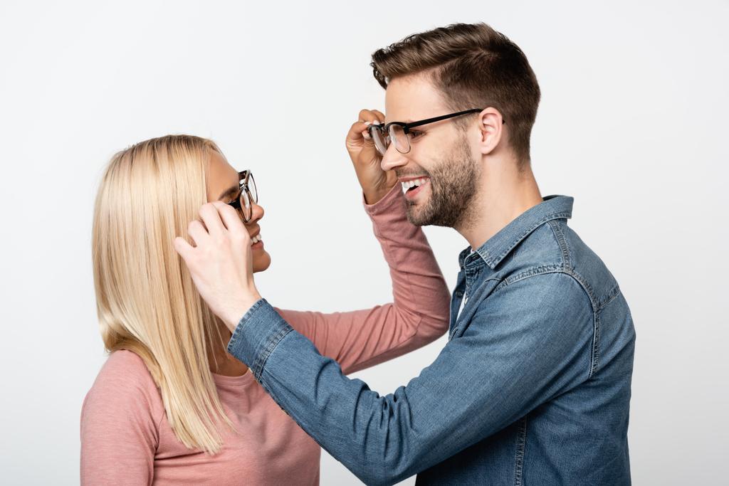 Usmívající se pár dotýkající se brýle jeden druhého izolované na šedé - Fotografie, Obrázek
