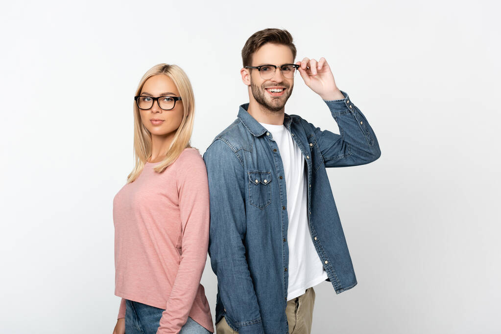 glimlachende man aanraken optische bril in de buurt blonde vriendin geïsoleerd op grijs - Foto, afbeelding